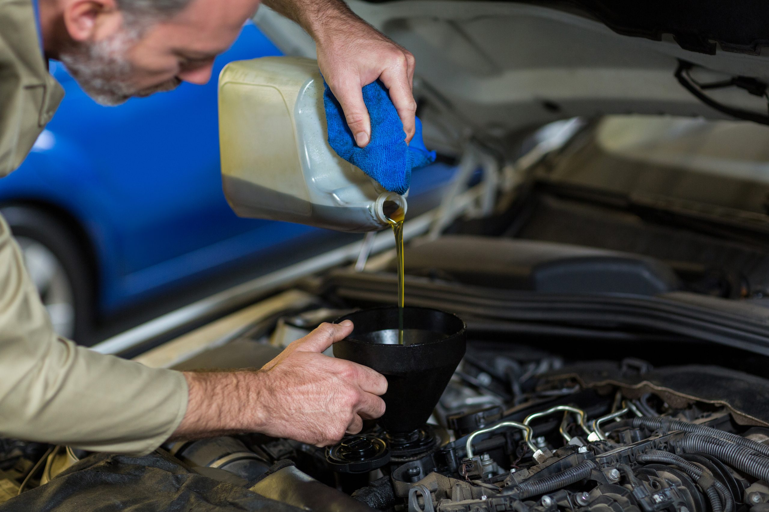 Mechanic pouring oil into car engine Mechanic pouring oil into car engine in repair garage